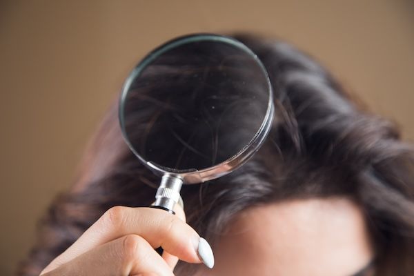 Giovane donna che esamina i suoi capelli con una lente d'ingrandimento