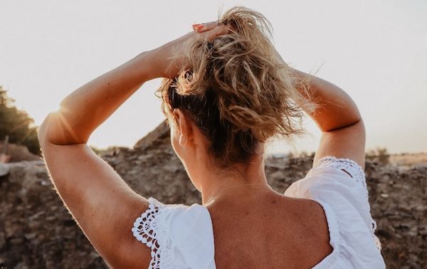 Vista posteriore di una donna matura che lega i capelli mentre si trova sulla spiaggia contro il cielo