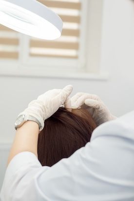 Medico dermatologo che esegue un esame per la perdita di capelli su una paziente con capelli lunghi e scuri Diagnosi delle malattie dei capelli e del cuoio capelluto Primo piano delle mani guantate del medico