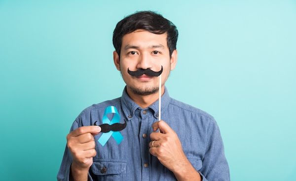 "Uomo bello che posa tenendo un nastro azzurro chiaro e un baffo."