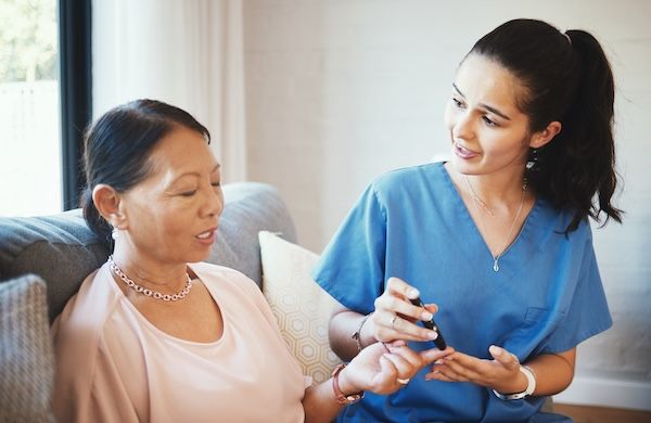Dottoressa e paziente anziano con diabete per iniezione di insulina o penna nel dito in assistenza domiciliare per anziani. Infermiera o assistente medico che esegue una puntura con ago per diabetici per cure mediche.