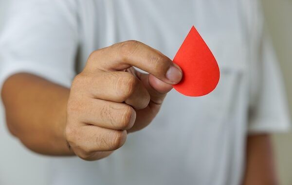 Una mano di un uomo sostiene una goccia di sangue di donatore con sfondo bianco.