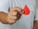 Una mano di un uomo sostiene una goccia di sangue di donatore con sfondo bianco.