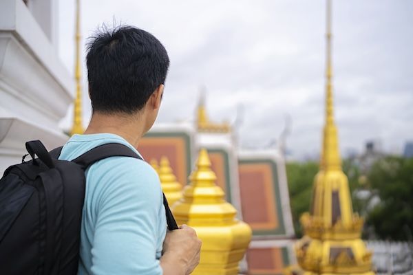 A un giovane asiatico con zaino piace molto visitare i templi thailandesi durante le vacanze estive a Bangkok.