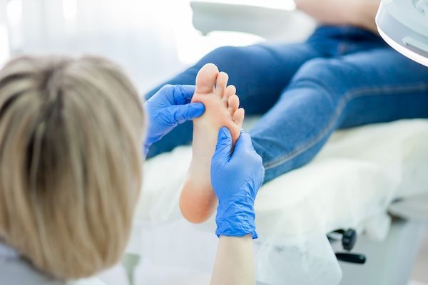 Medico podologo che controlla piedi e unghie di una paziente con alluce valgo 
