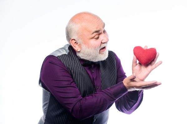 **Cura della salute. Un uomo anziano calvo e barbuto tiene in mano un cuore rosso. Prevenzione degli infarti. Problemi cardiaci e assistenza medica. Uomo maturo con cuore di San Valentino. Innamorarsi. Diagnosi e trattamento dell'aritmia cardiaca negli anziani