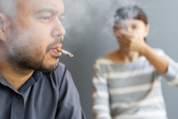 Marito che fuma sigarette e moglie soffocata dal fumo. L'uomo fuma sigarette e la donna si copre il viso con molto fumo intorno, che sa di inquinamento. Campagna passiva per smettere di fumare sigarette.