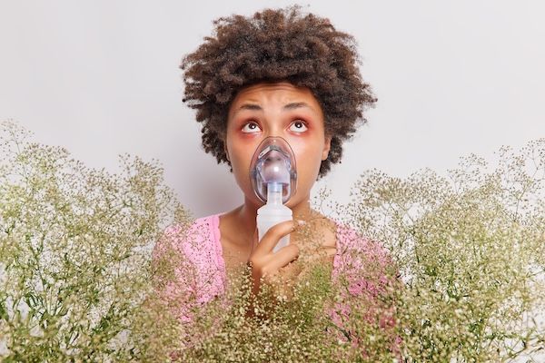 La donna usa un nebulizzatore inalatore che l'aiuta a respirare essendo allergica ai fiori selvatici. Ha gli occhi rossi e gonfi come reazione all'allergene, centrata nelle posizioni anteriori su sfondo bianco.