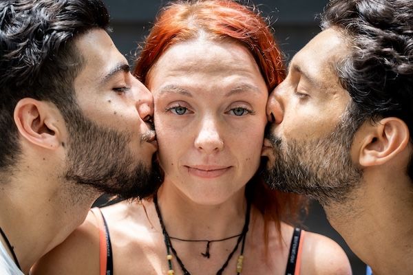 Due ragazzi di etnie diverse che baciano sulla guancia una ragazza in piedi al centro.
