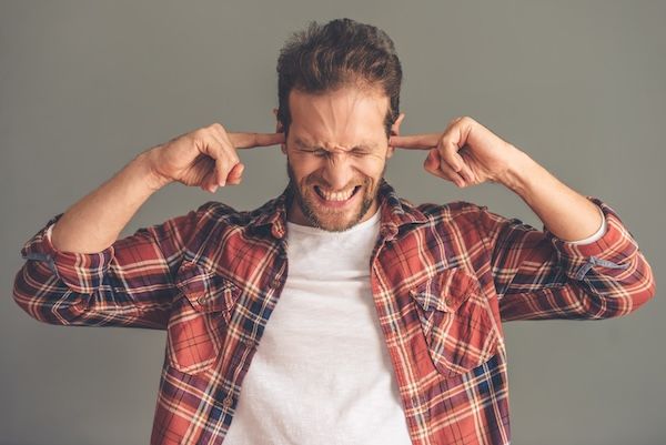 Giovane in abbigliamento casual si copre le orecchie per via di una perdita d'udito improvviso