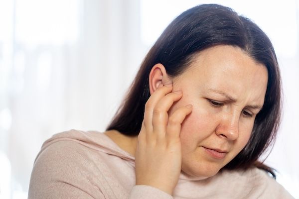 Giovane donna ha mal di testa, emicrania, stress e rumore di tinnito che fischia nelle orecchie, sintomi di perdita d'udito improvviso