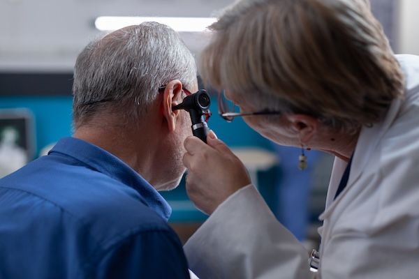 Dottoressa che tiene un otoscopio per eseguire una visita all'orecchio su un anziano durante un appuntamento medico a seguire di una perdita di udito improvviso. Otologo con strumento di otologia per effettuare esami e fornire consigli medici al paziente malato.