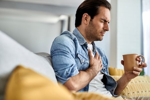 Giovane che si sente male e si tiene il petto con dolore al petto mentre beve tè nel soggiorno pericardite cos'è