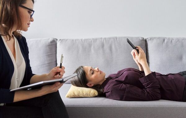 Giovane donna in consultazione con uno psicologo. Paziente di sesso femminile sdraiata sul divano, parla di problemi mentali e traumi. Assistenza professionale e supporto di psicologo, psichiatra o psicoterapeuta.