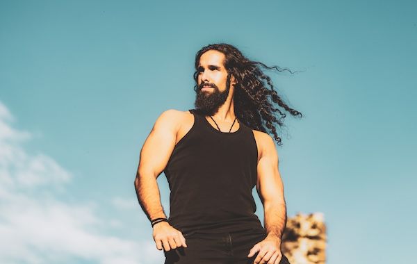 Bell'uomo barbuto con capelli lunghi e scuri risultati da un trapianto di capelli, uomo alla moda con capelli lunghi e ondulati e corpo forte e sano.
