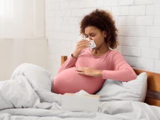 Donna in gravidanza malata che soffia il naso nel fazzoletto con sintomi da scarlattina