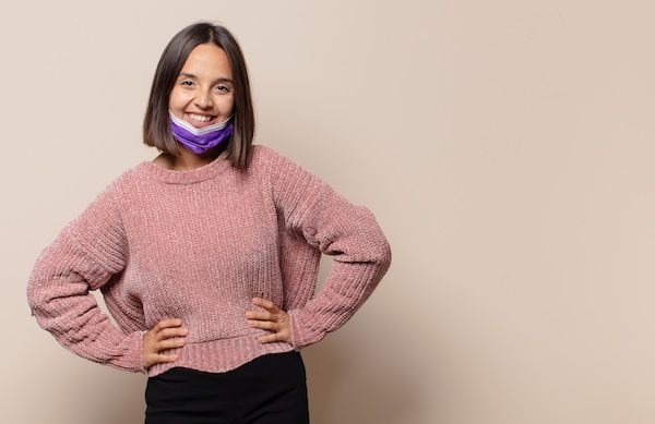 Giovane donna che sorride felicemente con una mano sul fianco e un atteggiamento sicuro, positivo, orgoglioso e amichevole.