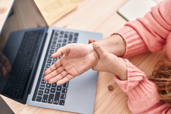 Giovane e bella donna ispanica che lavora nel commercio elettronico e soffre di dolore al polso in ufficio a causa di una frattura allo scafoide non curata