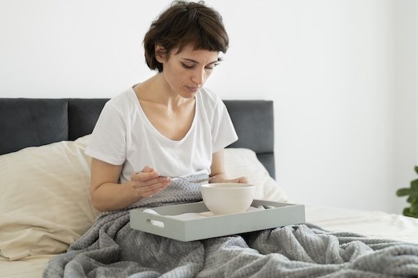 donna malata a letto mangia zuppa per fare abbassare la febbre alta