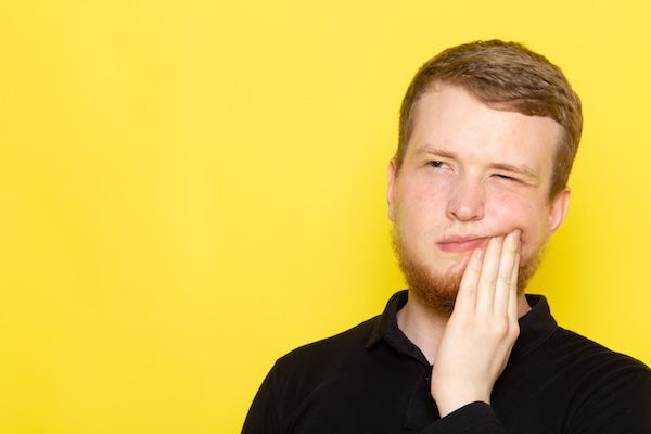 Vista frontale del giovane uomo in camicia nera che posa con un'espressione di dolore a un dente o ad una gengiva a causa di un ascesso gengivale che scoppia da solo