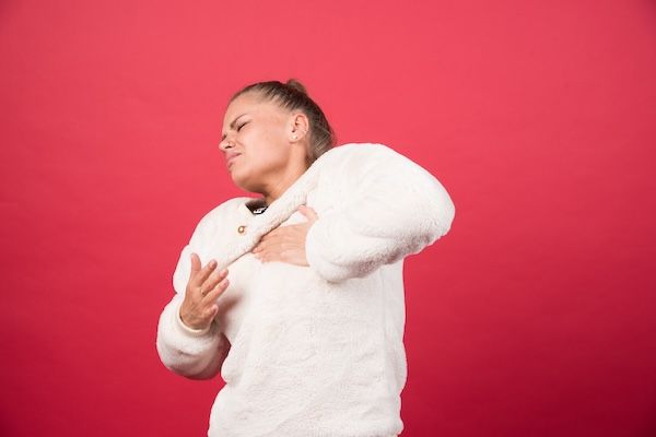 Foto di una donna con sintomi di bronchite senza febbre che si tocca il petto con la mano per dolore alle vie respiratorie