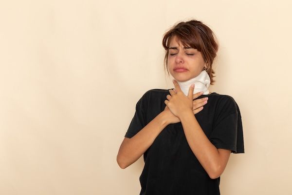 Vista frontale di una giovane donna malata con alta temperatura che si copre la gola, sentendosi male, alla scrivania bianca.
