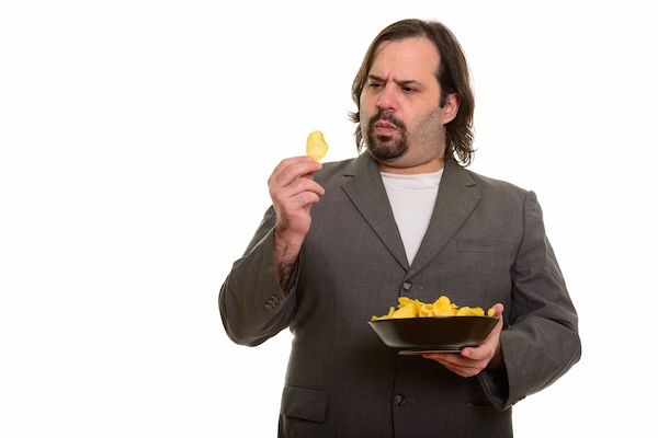 Uomo d'affari caucasico in carne che tiene una ciotola di patatine fritte uno dei cibi da evitare per chi soffre di colesterolo alto