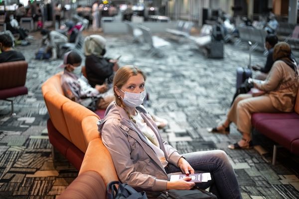 Donna con mascherina protettiva seduta al terminal dell'aeroporto in attesa del volo. Viaggi e turismo durante la pandemia di coronavirus covid eg 5 sintomi