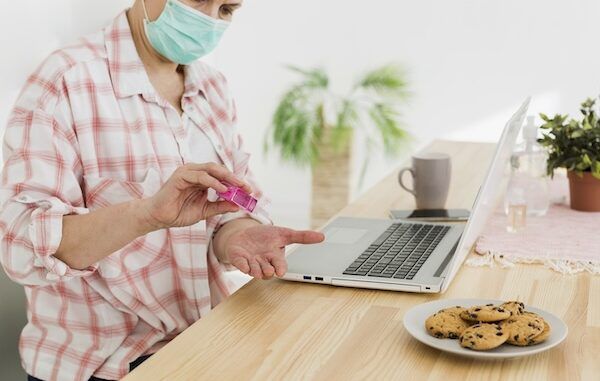 Vista laterale dell'anziana che disinfetta le mani prima di usare il computer portatile per prevenire il covid eg 5 e sintomi