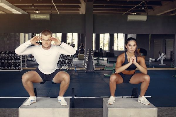 Coppia sportiva durante un allenamento in abbigliamento tecnico in palestra fa squats