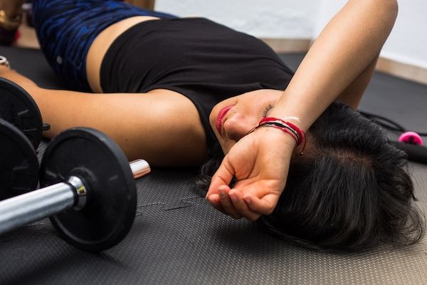 Primo piano di una donna esausta sdraiata a terra dopo l'esercizio e l'allenamento perché il tempo di recupero è importante per una dieta e aumentare la massa muscolare senza ingrassare