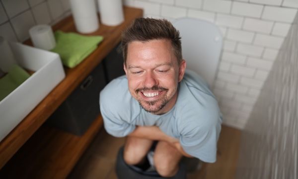 Uomo con un sorriso soddisfatto seduto sul water per via di una gran bella motilità intestinale
