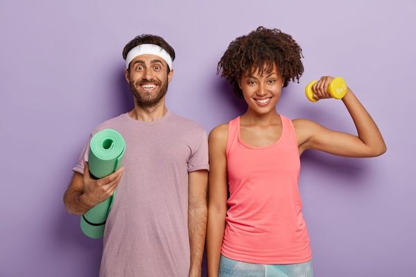 Donna allegra e uomo di diversa nazionalità, fianco a fianco, portano tappetini da yoga e sollevano manubri. concetto di motilità intestinale regolare