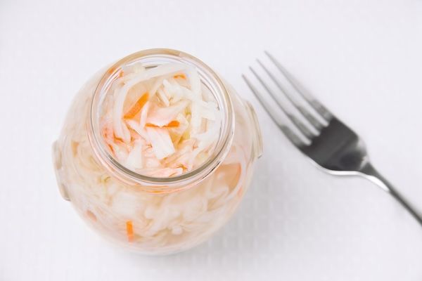 Cavolo in aceto con carote in un barattolo su uno sfondo bianco, accanto a una forchetta. Verdure fermentate buone per evitare problemi intestinali