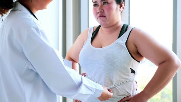 Una dottoressa misura la vita di una donna sovrappeso preoccupata nella stanza dell'ospedale per i diversi tipi di obesità