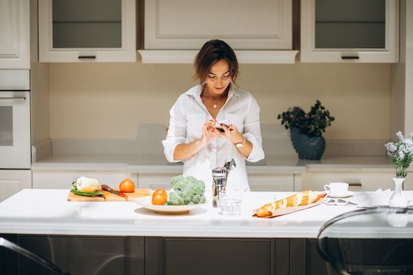 Giovane donna in cucina che prepara la colazione con una dieta per abbassare il colesterolo alto e parla al telefono.