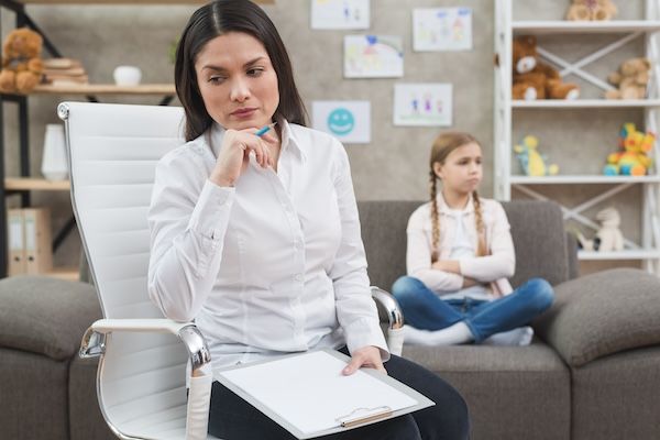 Psicologo riflessivo che tiene in mano una matita e una tavoletta colorate di blu, seduto di fronte a una ragazza triste che è seduta sul divano non sa cos'è l'adhd