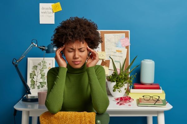 La donna stanca e irritata tiene entrambe le mani sulle tempie, aggrotta le sopracciglia e si sente sopraffatta dopo aver lavorato a lungo perché non sa cos'è l'ADHD