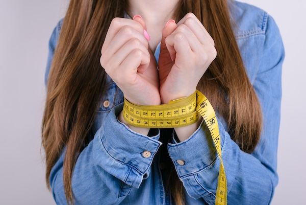 Foto in primo piano ritagliata del disagio triste e infelice di una persona che conduce uno stile di vita poco salutare, con le mani giunte, su uno sfondo grigio isolato. la psicologia è tra le cause dell'anoressia