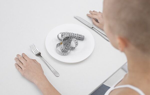 Giovane donna con un disturbo alimentare con un metro da sarta nel piatto tra le cause dell'anoressia