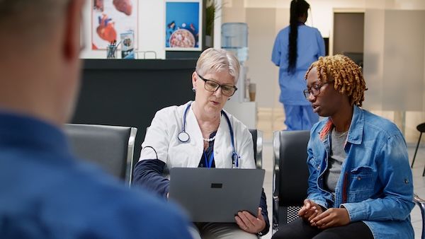 Un medico senior mostra la diagnosi sul portatile al paziente malato, spiegandogli la malattia e il trattamento farmacologico durante la visita di controllo nella sala d'attesa. Medico e donna parlano della differenza tra dialisi e emodialisi