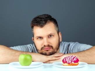 Un uomo adulto sceglie tra una ciambella e una mela verde. Concetto di resistenza alla tentazione, cibo veloce, cibo sano, dieta, cura del corpo e dieta per abbassare il colesterolo alto