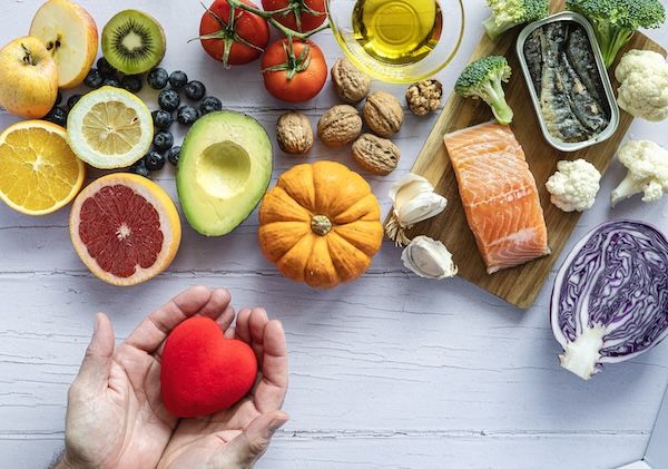 Due mani che tengono un cuore rosso circondato da frutta fresca, verdura e pesce. Prevenzione delle malattie e dieta per il colesterolo alto