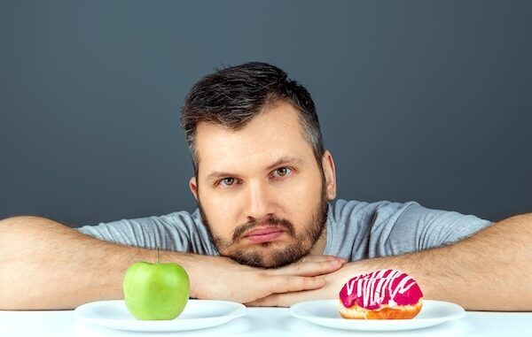 Un uomo adulto sceglie tra una ciambella e una mela verde. Concetto di resistenza alla tentazione, cibo veloce, cibo sano, dieta, cura del corpo e dieta per abbassare il colesterolo alto