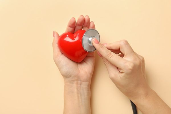 Mani femminili che tengono un cuore e uno stetoscopio su una superficie beige concetto di prevenzione dello pacemaker