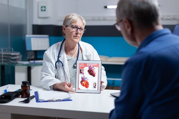 Medico che spiega la diagnosi di cardiologia con l'immagine del cuore su un tablet al paziente. Medico generico che mostra illustrazioni sul sistema cardiovascolare e sulla struttura anatomica dell'uomo prima di un pacemaker