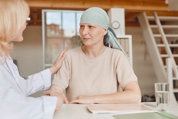 Ritratto in toni caldi di una donna calva matura che parla con la dottoressa, confortandola e congratulandosi con lei durante la consulenza sulla guarigione dall'alopecia e dal cancro, grazie a terapia genica tumori