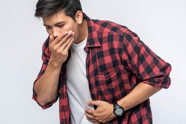 uomo in piedi con mal di stomaco mette le mani sullo stomaco e si copre la bocca