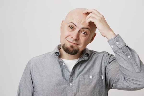 uomo sorridente che si gratta la testa calva pensieroso