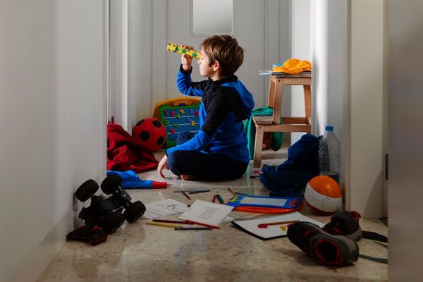 Bambino seduto sul pavimento di un corridoio pieno di cose sparse sul pavimento - Che cos'è l'ADHD nei bambini